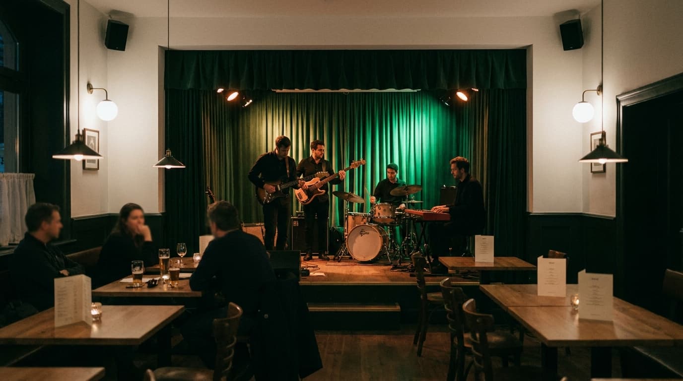 A live band on a small stage at dusk, warm lights, viewed from the back of a calm room